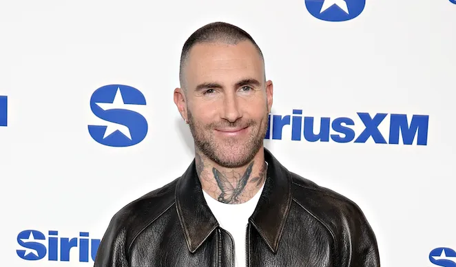 Adam Levine smiling on the set of a music competition show