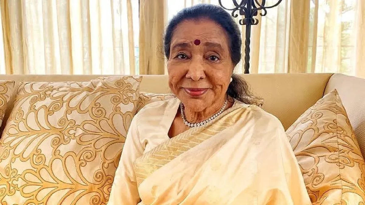 A close-up portrait of the iconic Indian singer Asha Bhosle, smiling warmly.