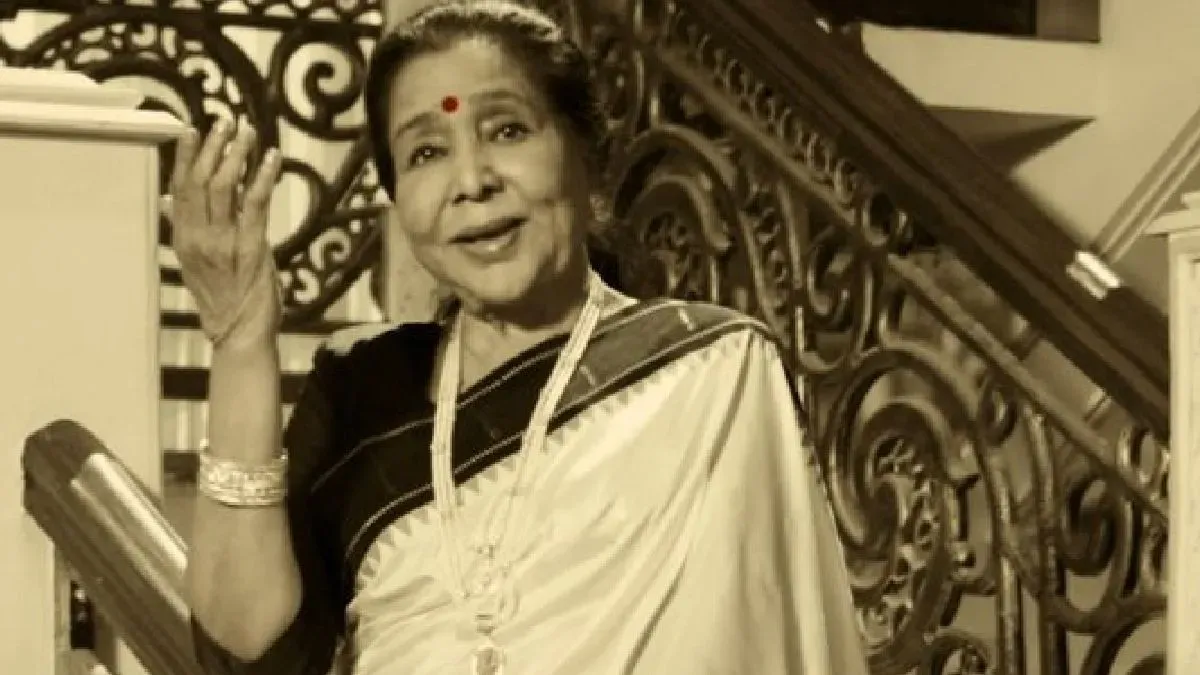 A smiling Asha Bhosle with her signature elegant hairstyle, likely from a performance or public appearance.