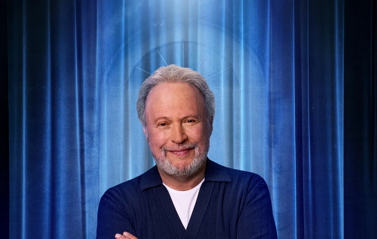 Billy Crystal smiling on a stage with warm lighting