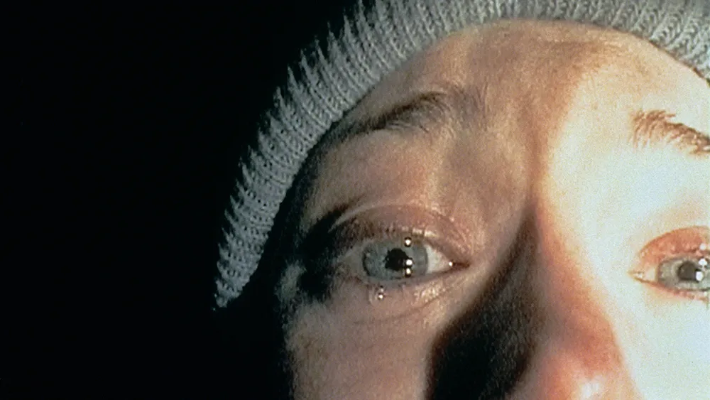 A shadowy figure in a dark forest, reminiscent of The Blair Witch Project's eerie aesthetic.