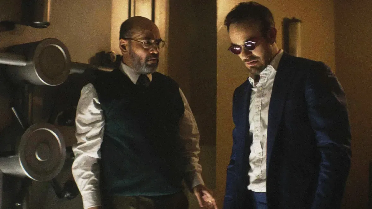 Charlie Cox as Daredevil standing in a dark, red-lit alleyway in New York city.