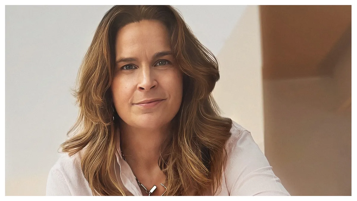 A professional woman, Sara May, smiling and looking confident in a business setting.