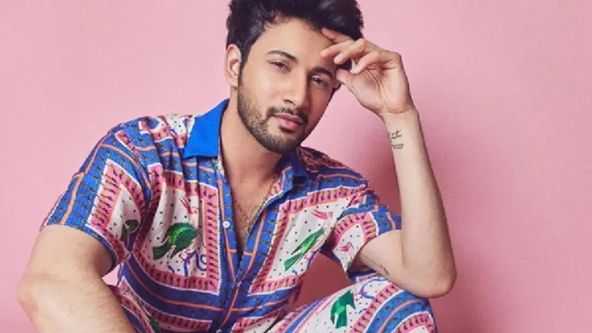 A man wearing a vibrant floral shirt, with another man in a colorful Bandhani jacket in the background, showcasing new men's fashion trends.