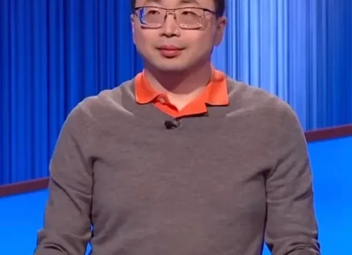 Jamie Ding on the Jeopardy! stage, smiling next to the host, with the game board behind them.