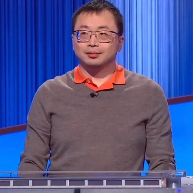 Jamie Ding on the Jeopardy! stage, smiling next to the host, with the game board behind them.