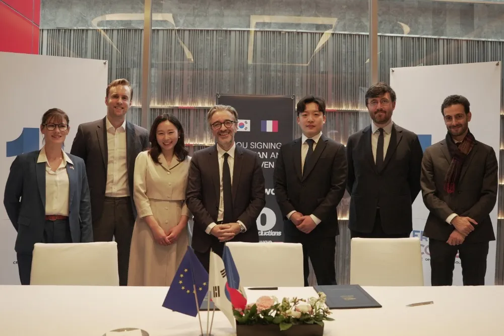 French and Korean executives shaking hands during a formal signing.