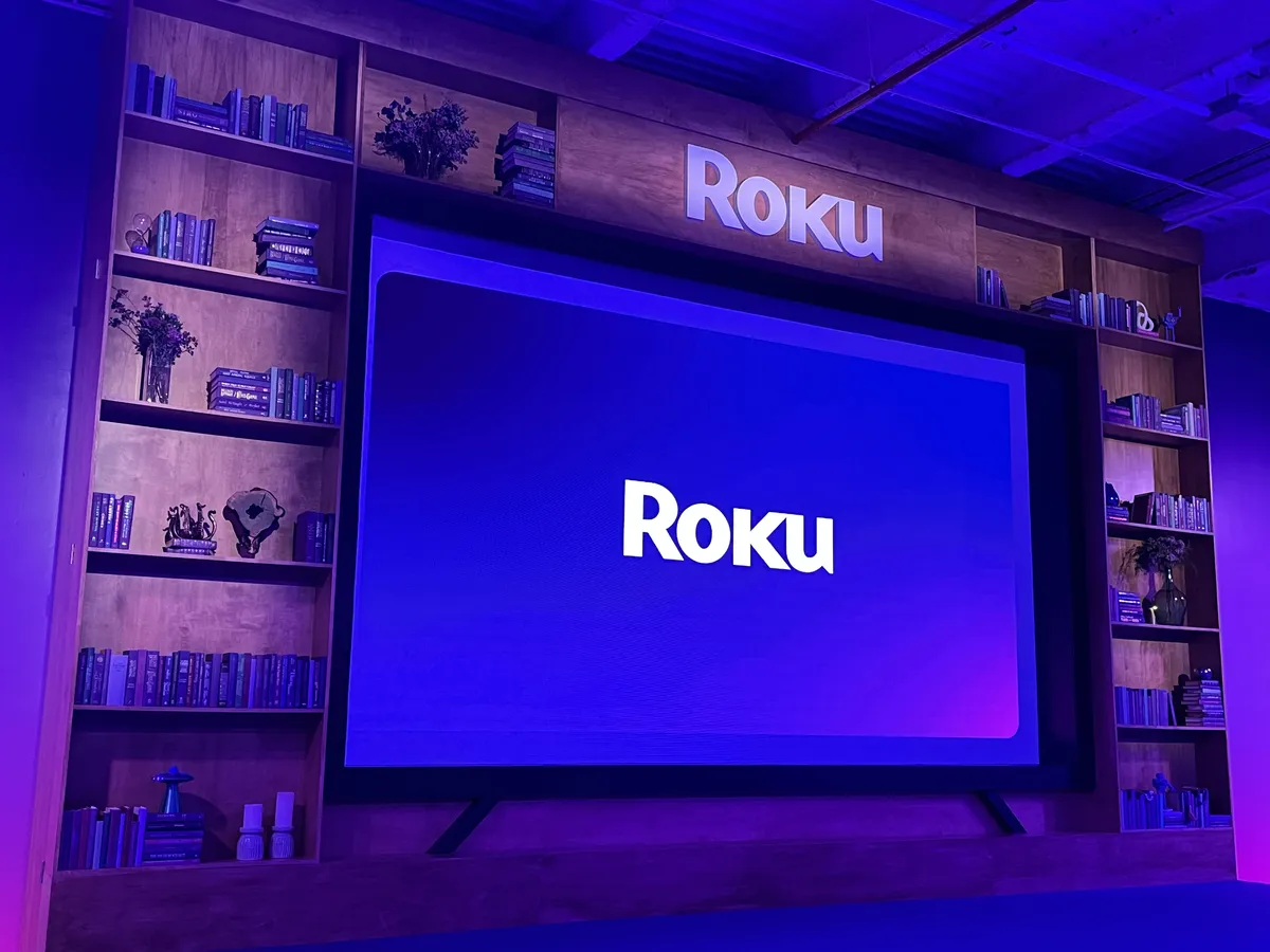 A person holding a Roku remote in front of a TV.
