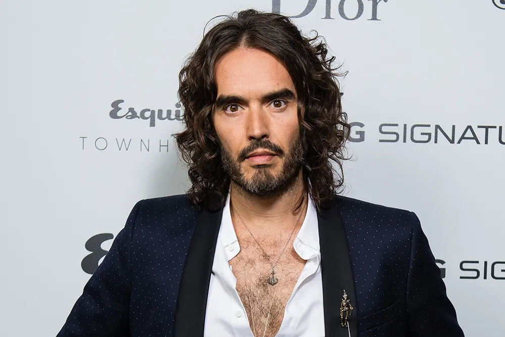 Russell Brand, looking serious, speaking during an interview.