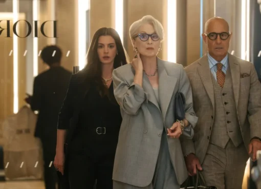 A stylish woman in a designer coat walking through a busy office.