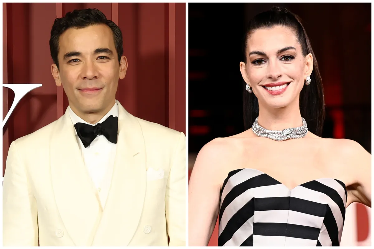 Anne Hathaway and Conrad Ricamora smiling and talking on a movie set, dressed in casual clothes.