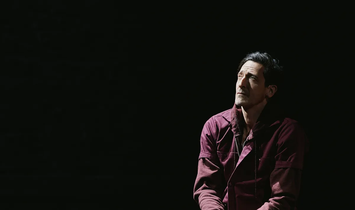 Adrien Brody performing on a dark, moody Broadway stage