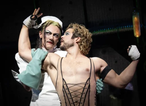 Luke Evans performing on stage in a theatrical costume with bright neon lights