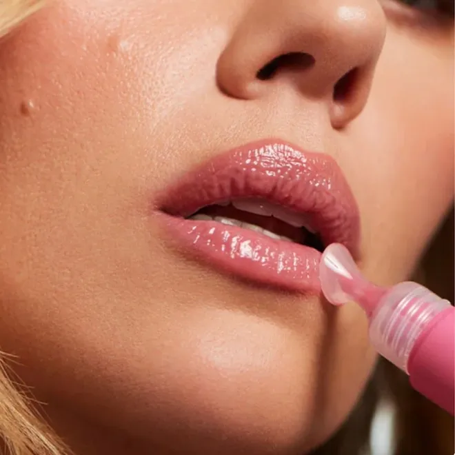 A close-up shot of shiny pink lip gloss being applied to a model's lips.