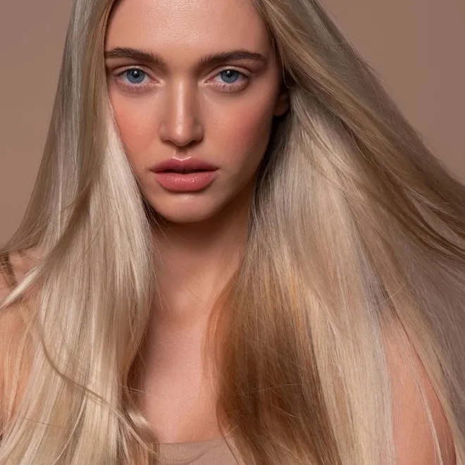 A smiling woman with perfectly smooth, sleek, and frizz-free dark hair, looking confident as she steps out of a doorway into a slightly humid outdoor setting.
