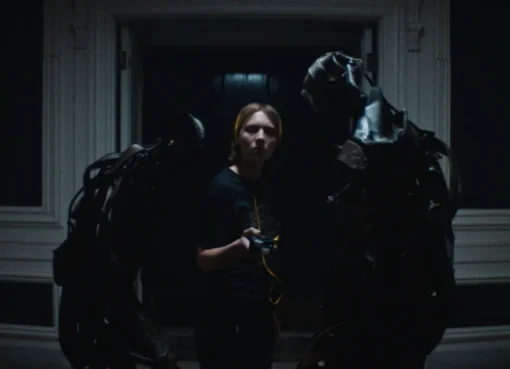 A dark, moody still from the horror film 'Recluse' showing a lone figure in a dimly lit, confined space.