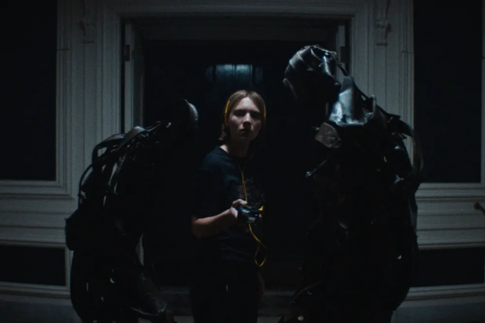 A dark, moody still from the horror film 'Recluse' showing a lone figure in a dimly lit, confined space.