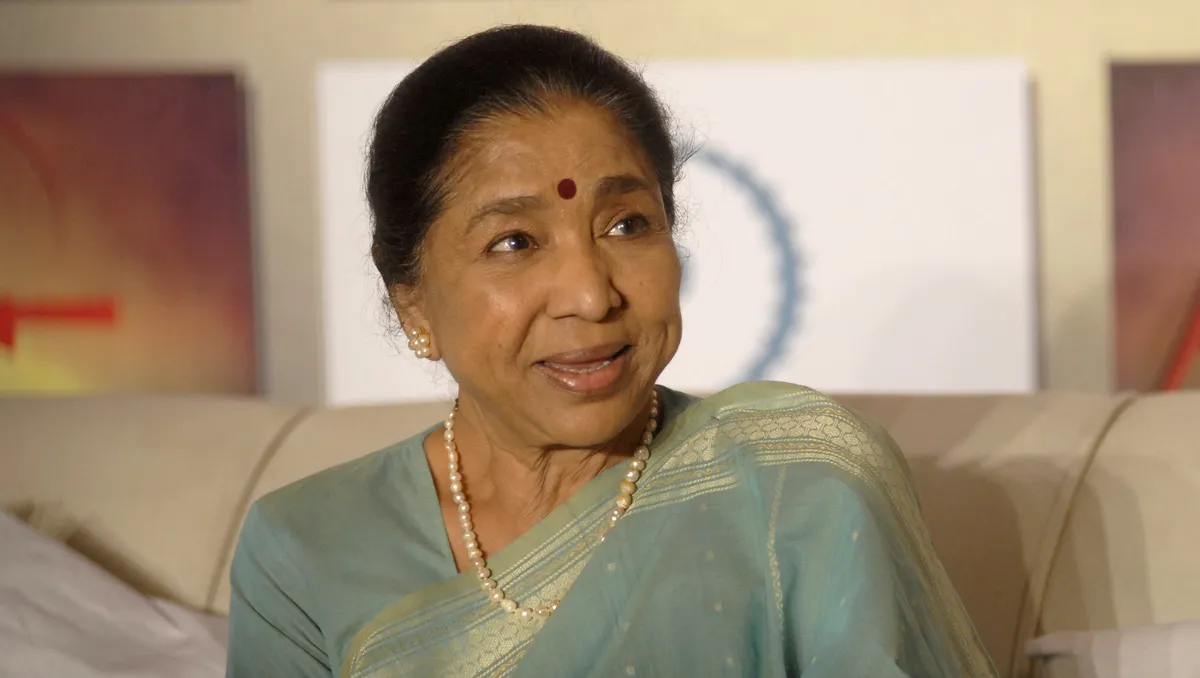 A smiling Asha Bhosle singing into a microphone, radiating joy.