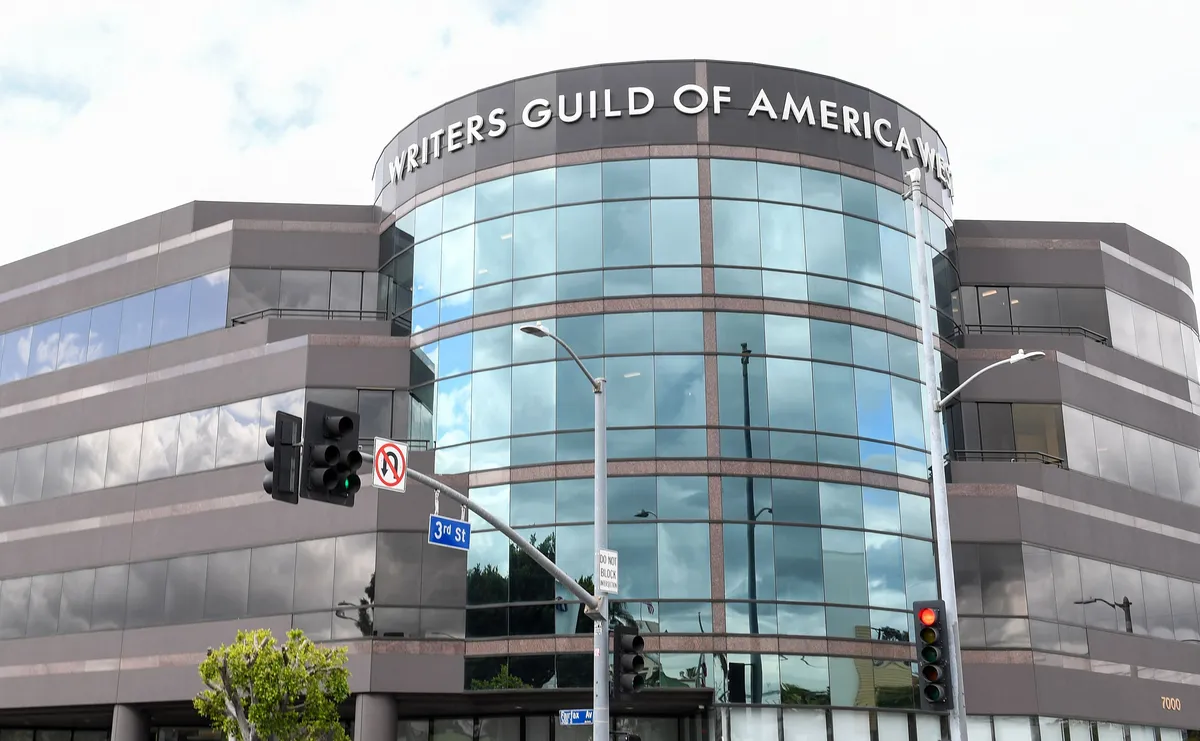 People holding protest signs in front of a Hollywood studio building