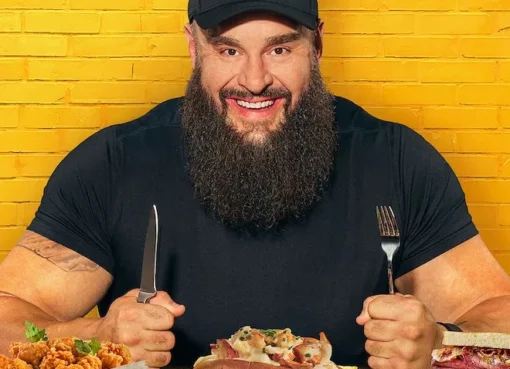 Braun Strowman, a muscular WWE wrestler, smiling while holding a plate of food.