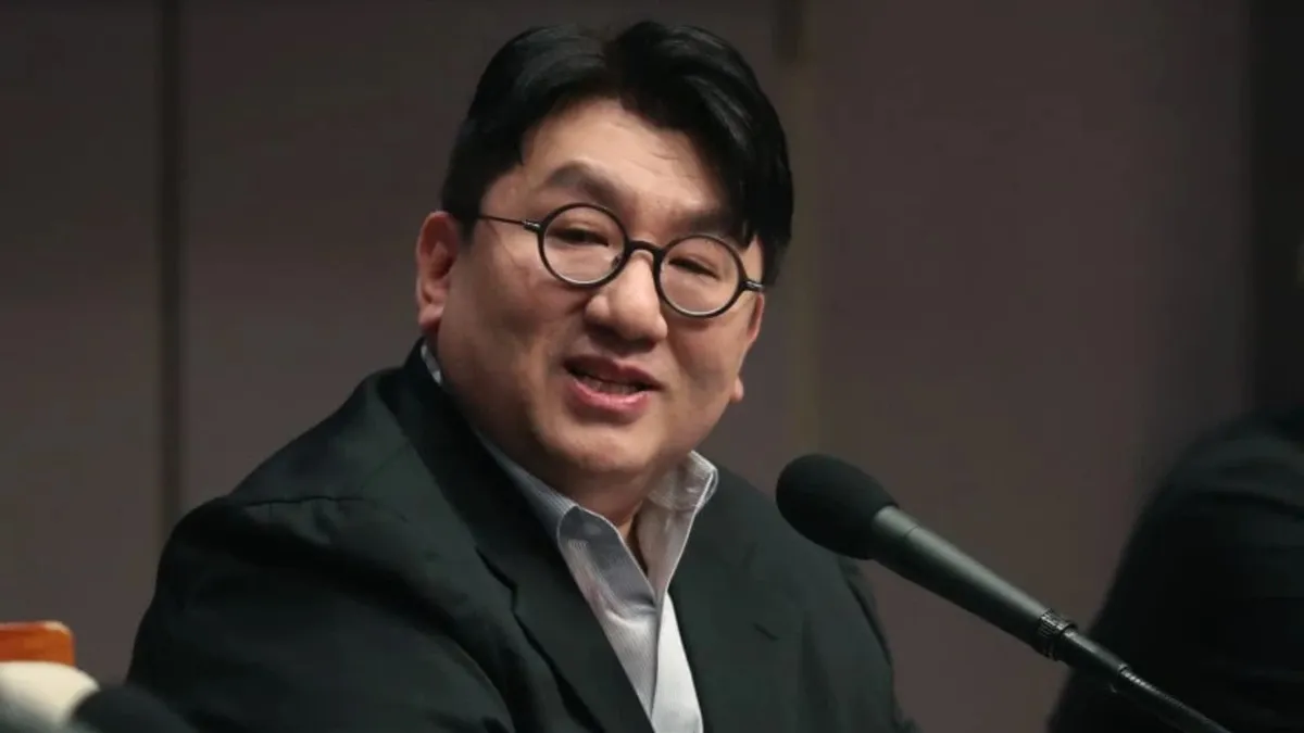 Bang Si-Hyuk standing in front of a modern background