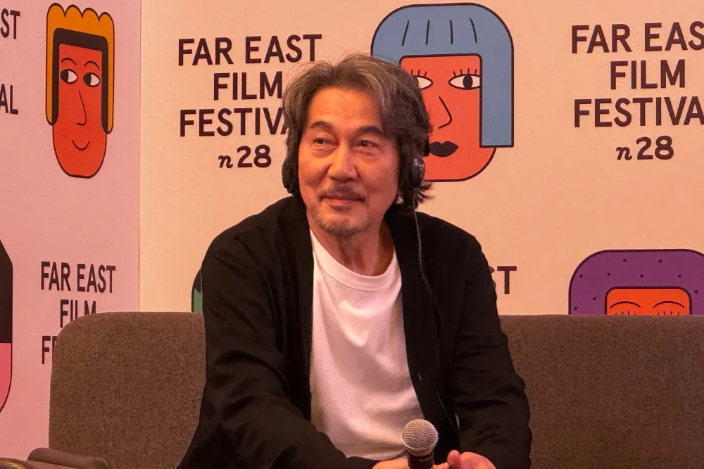 Koji Yakusho smiling, possibly on a film set.