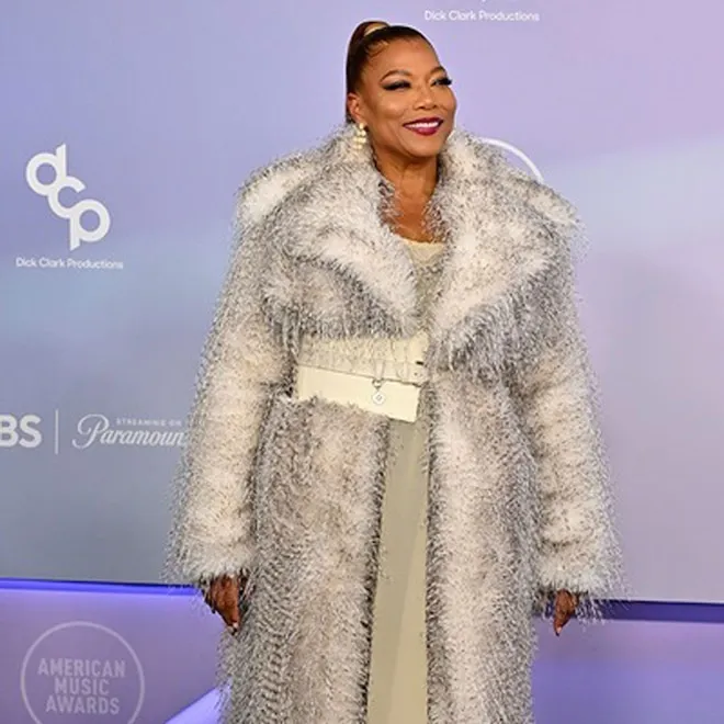 Queen Latifah on stage at the American Music Awards, holding a microphone, with a vibrant stage background.