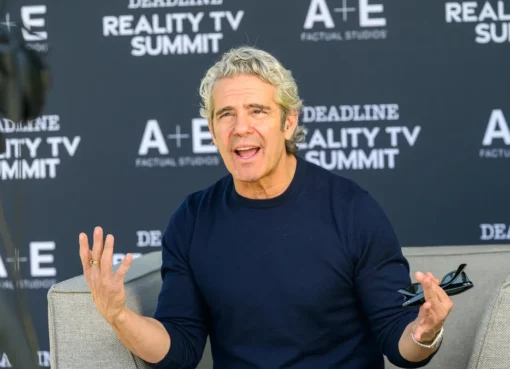 Andy Cohen smiling and gesturing on a talk show set.