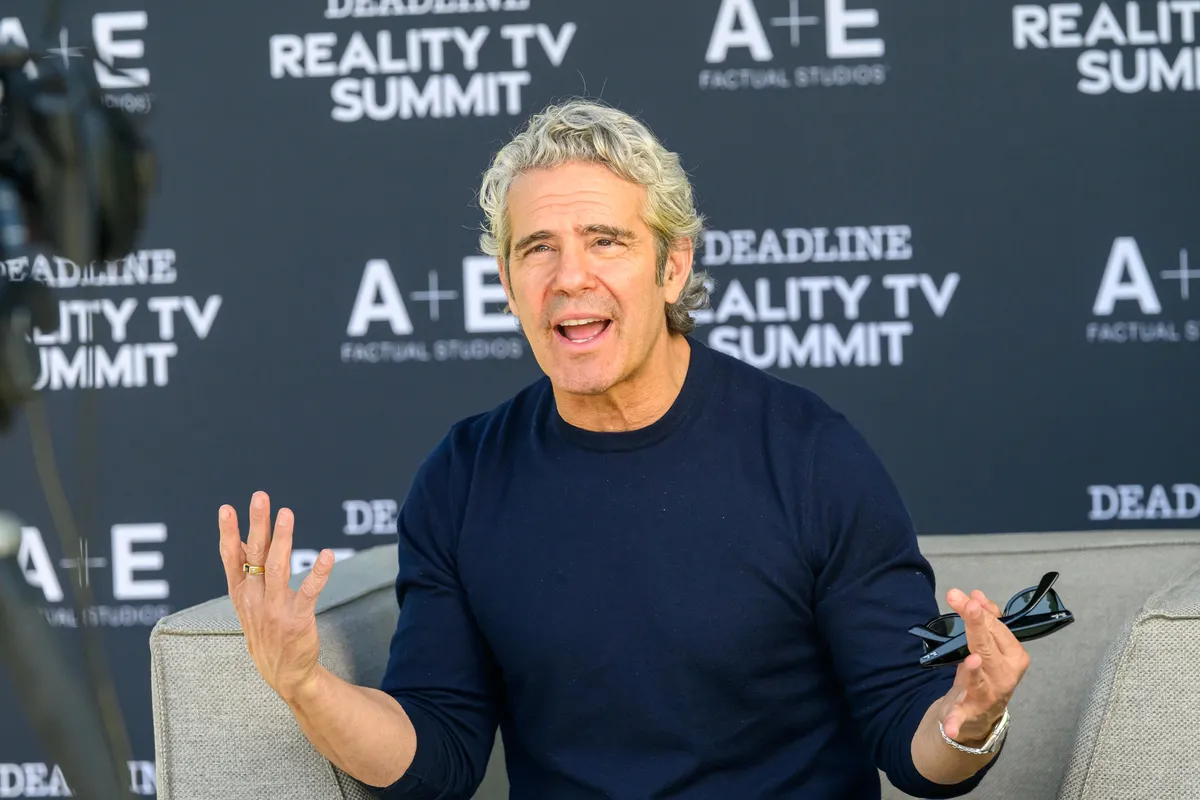 Andy Cohen smiling and gesturing on a talk show set.