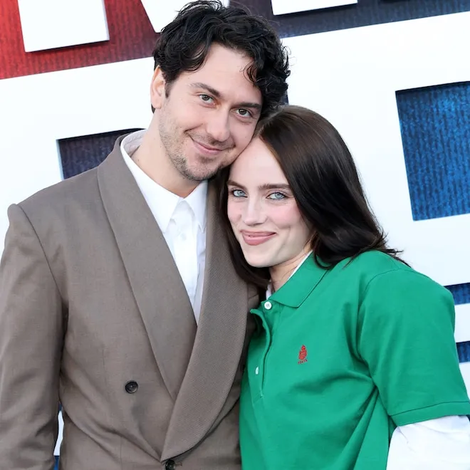 Billie Eilish and Nat Wolff smiling together on a red carpet at her movie premiere.
