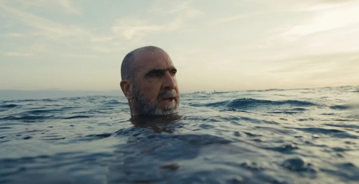 Close-up portrait of Eric Cantona with a serious, intense expression.