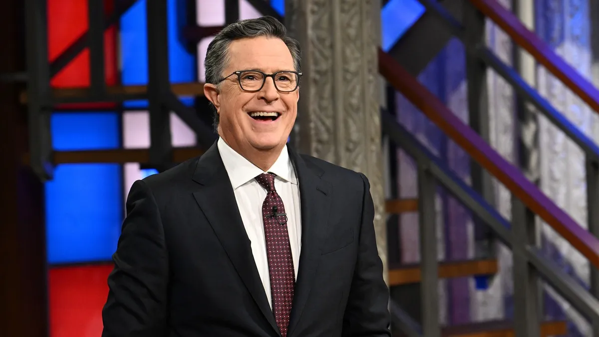 Stephen Colbert smiling at a party with a 'Fired and Festive' theme.