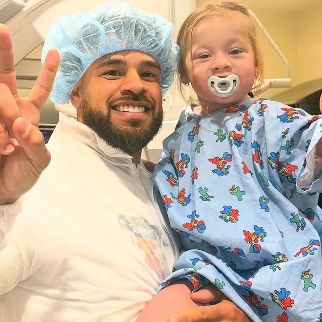 Cory Wharton holding his young daughter Maya in a hospital room