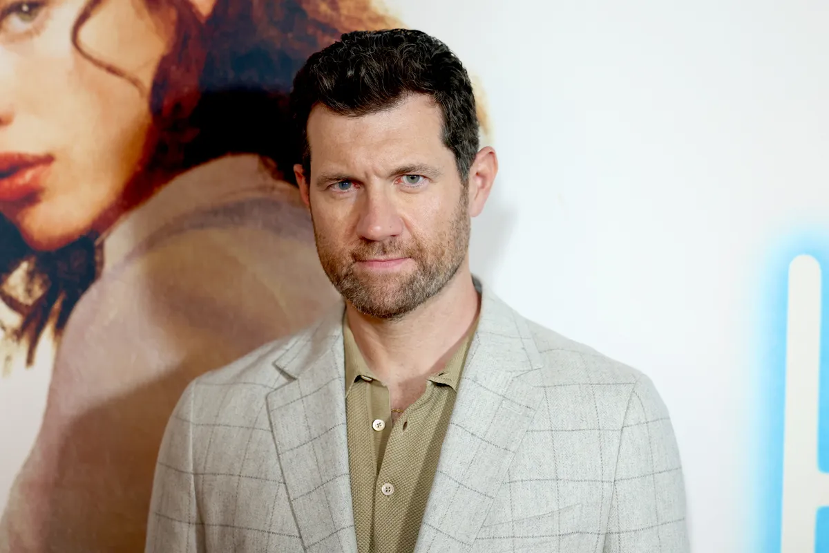 Billy Eichner smiling and holding a microphone, possibly in a street setting.
