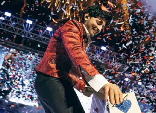 Darshan Raval singing on stage with a microphone, surrounded by vibrant stage lights and a cheering crowd.