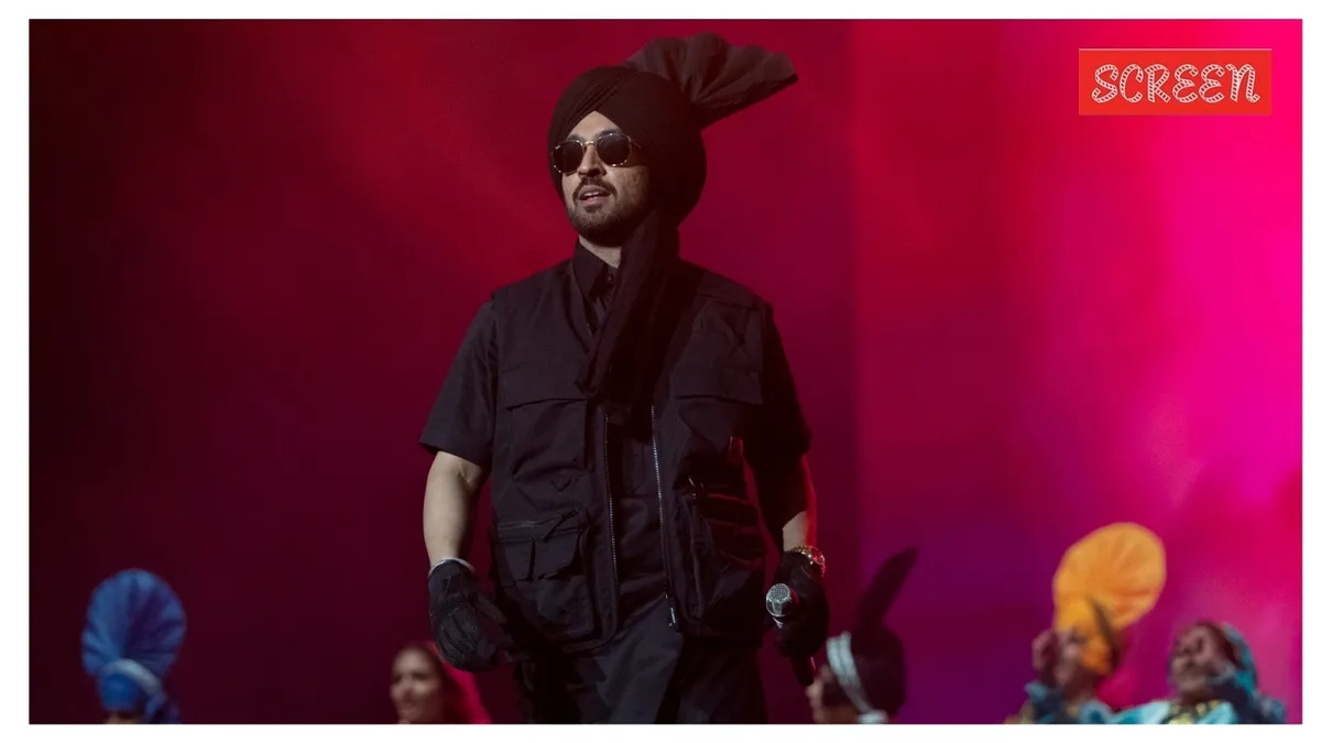 Diljit Dosanjh singing on stage with bright lights and a colorful turban.