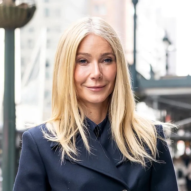 Gwyneth Paltrow smiling with a bunch of fresh arugula.