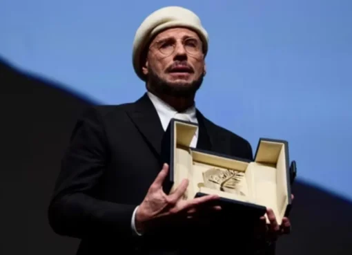 John Travolta looking happy and emotional while holding an award at the Cannes Film Festival.