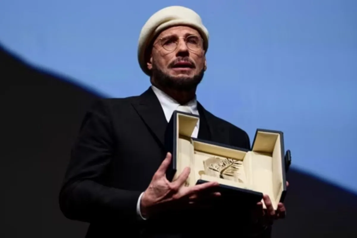 John Travolta looking happy and emotional while holding an award at the Cannes Film Festival.