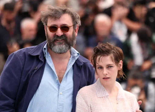 Kristen Stewart smiling and waving at the Cannes Film Festival red carpet.