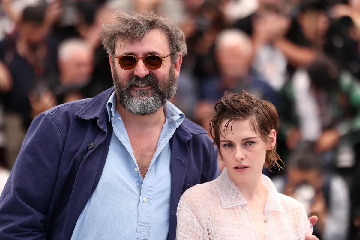 Kristen Stewart smiling and waving at the Cannes Film Festival red carpet.