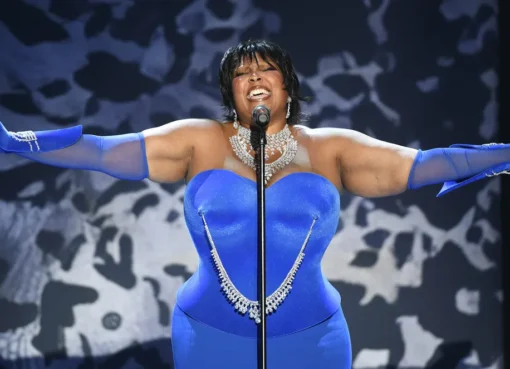 Lizzo performing on stage at the amfAR gala with an ocean view in the background.