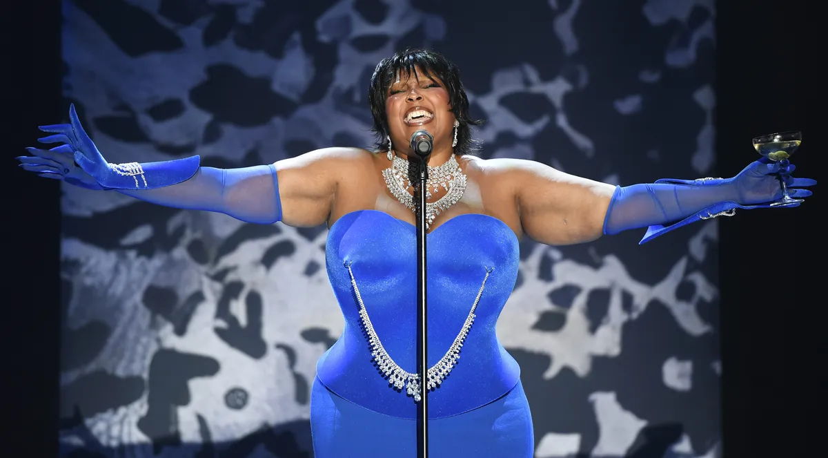Lizzo performing on stage at the amfAR gala with an ocean view in the background.