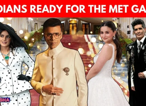 Karan Johar smiling, wearing a stylish, possibly maximalist outfit, with Met Gala branding subtly in the background.