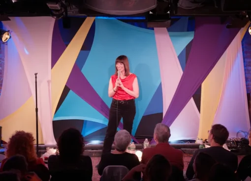 Comedian Ophira Eisenberg on stage, possibly holding a microphone.
