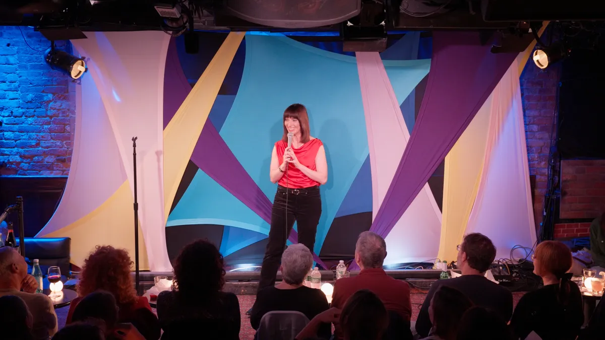 Comedian Ophira Eisenberg on stage, possibly holding a microphone.