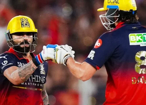 A crowd of jubilant Royal Challengers Bengaluru players lifting the IPL 2026 trophy, bathed in red and gold light.