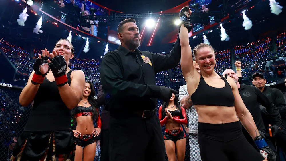 Ronda Rousey and Gina Carano facing off in a brightly lit fighting ring