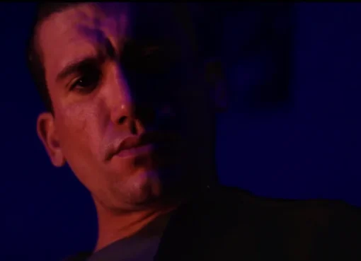 Jaime Lorente looking intense and serious in a dimly lit scene, possibly from a horror film.