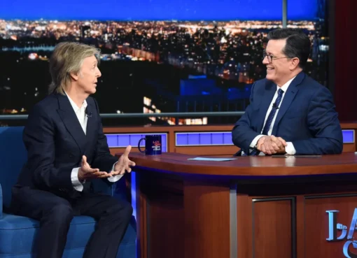 Stephen Colbert smiling on The Late Show stage with guests.
